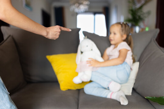Adult scolding young girl sitting on sofa with plush toy at home