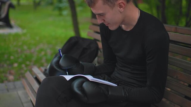 young boxer reading notebook on park bench, gloves resting on lap, studying tactics and notes, backpack beside seat, focused gaze, coachlike concentration, autumn leaves, urban calm, planning session