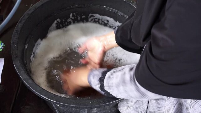 Woman hand washing clothes manually in black bucket with soapy water, daily household activity, simple lifestyle and domestic routine concept