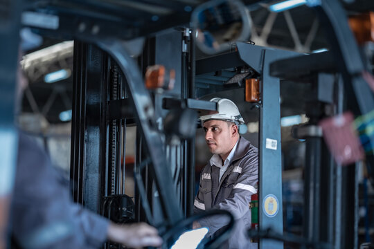 Caucasian male factory supervisor talking on radio with forklift driver in foreground. Industrial logistics and modern distribution facility management.
