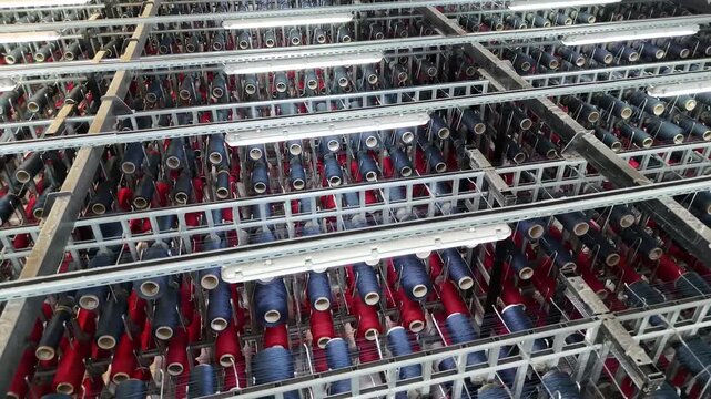 High-angle view of a large industrial textile creel holding numerous spools of red and blue yarn in a factory.