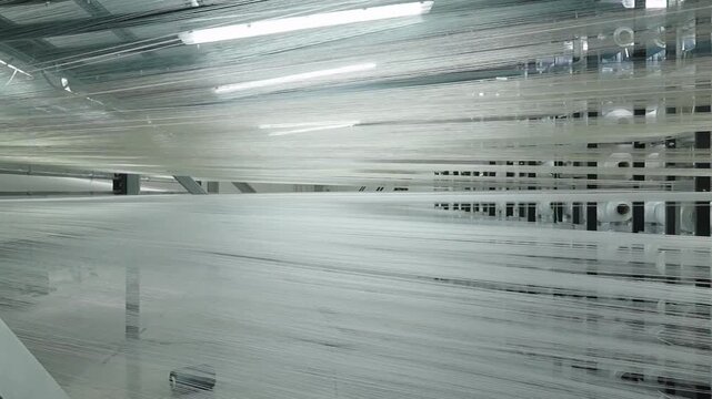 Close up of white synthetic fibers moving rapidly through an industrial weaving machine with a single red thread.