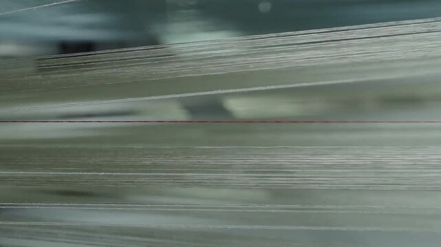 Close up of white synthetic fibers moving rapidly through an industrial weaving machine with a single red thread.
