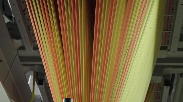 Close up of vibrant orange and yellow synthetic fibers moving through an industrial loom in a carpet factory.