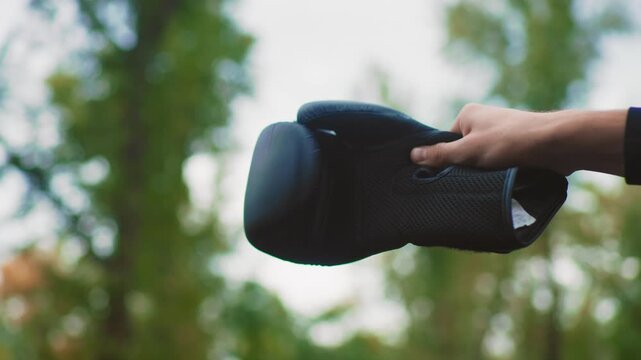 Hand offering black glove forest background, closeup of textured mesh mitt held by outstretched wrist, soft bokeh foliage, muted sunlight, tactile padding visible, subtle motion, peaceful outdoor