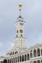 Naklejka premium The North River Terminal or Rechnoy Vokzal of Moscow, Russia. Historic clock tower topped by a Soviet golden star rises above neoclassical arches and statues against a cloudy sky, it was built in 1937