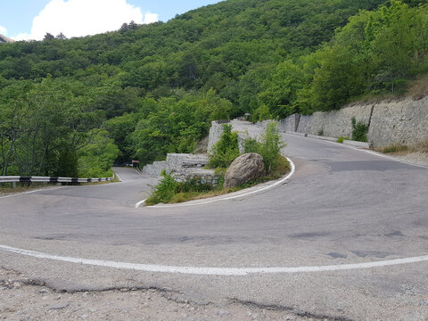 Winding asphalt road in mountain forest. Sharp curve on hair-pin turn highway. Summer landscape with green tree and stone wall. Travel and driving adventure concept in highland area.