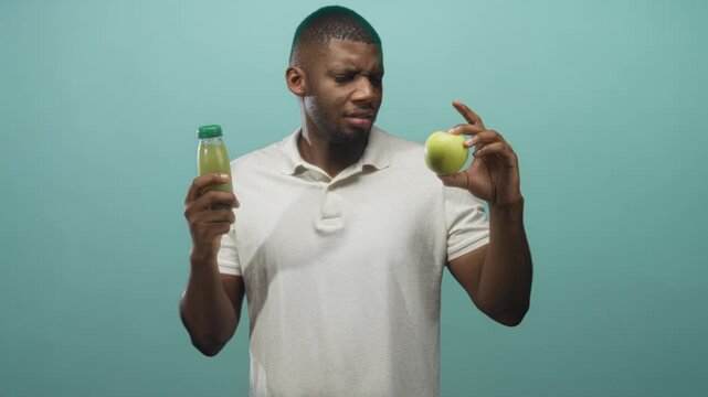 Man in beige polo grimaces with closed eyes while holding green apple and bottled juice in a mint studio; taste test skepticism.