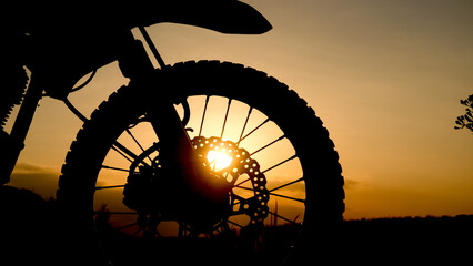 Silhouette of a Motorcycle's wheel with the sun shining through its spokes. The setting is a scenic landscape © Stock4u2024 