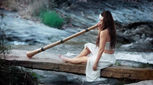 A serene moment by the river as a woman plays the didgeridoo, connecting with nature and immersing herself in the soothing sounds of the flowing water around her.