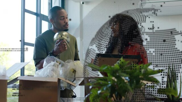 Colleagues opening boxes, male lifting brass object while female pointing frame, staging office