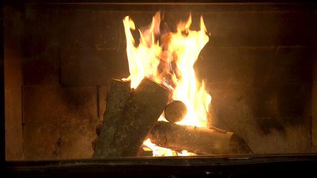 Close up shot of bright fire flames burning wood logs in a cozy indoor fireplace creating a warm and relaxing atmosphere for winter holiday season at a mountain cabin or home