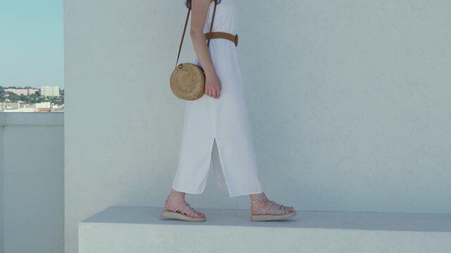 Woman in white dress and sandals walks on a rooftop with city view