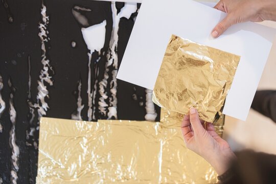 Hands gently apply shimmering gold leaf to a stunning piece of luxury furniture in a vibrant artist&rsquo;s studio, surrounded by creative chaos and rich colors