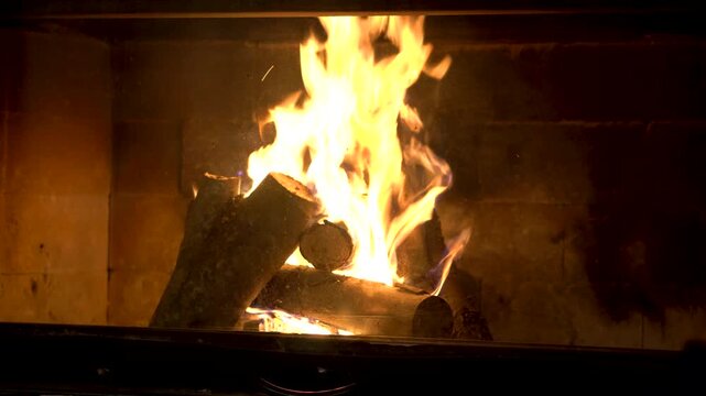 Close up shot of bright orange flames dancing on wooden logs inside a brick fireplace creating a warm and cozy atmosphere for winter nights at home or in a rustic mountain cottage
