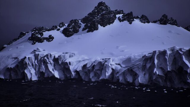 dusk lit antarctic iceberg towering over sea, dramatic cliff faces and crevassed snowfields under heavy indigo sky, raw texture and frigid atmosphere ideal