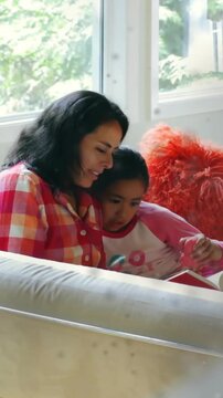 Vertical video: Mom guiding daughter reading, girl tapping red book sparking animated text learning