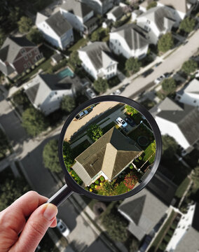 Aerial view new homes in a housing development with a hand and magnifying glass -- home ownership and house buying concept
