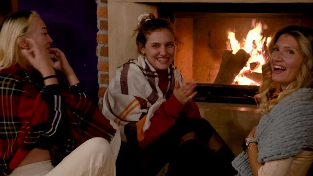 Smiling young woman enjoying a warm fireside moment, chatting with friends in a cozy living room, capturing natural emotions and relaxed winter lifestyle atmosphere