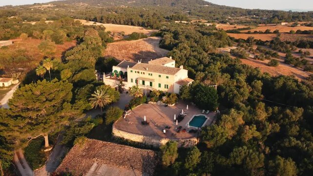 Aerial view of a traditional Spanish Mediterranean house with a pool situated on a hill, at sunset in the summer