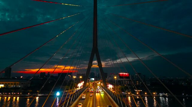 night view of symmetric modern Rama VIII cable-stayed bridge over Chao Phraya river in Bangkok, perspective of suspension urban span connecting city skyline across Thai waterway, aerial drone view 4k