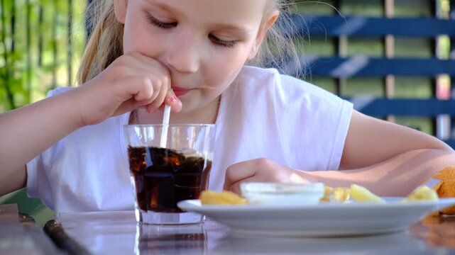 Child pretty girl drinking cold fizzy beverage cola from glass cup, close up