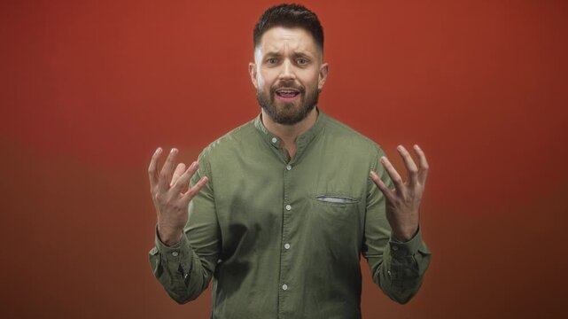 Hispanic man with beard raising hands and speaking in a red studio, open palms and animated expression; frustration.