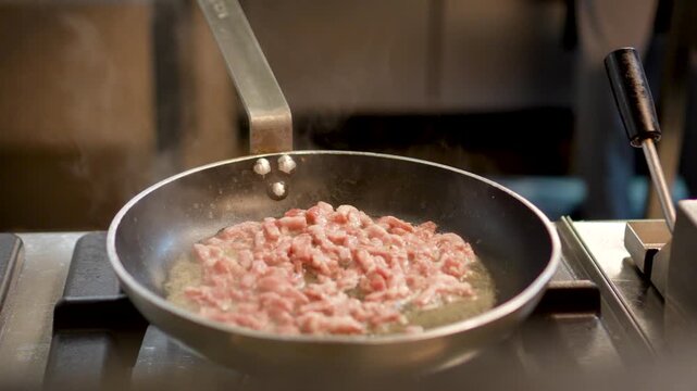 The chef in the restaurant is frying bacon in a large pan