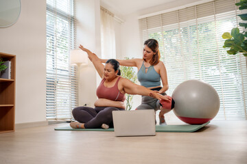 Obraz premium Physical therapy assisted stretch personal trainer home workout yoga mat exercise ball seated pose laptop living room adult woman practicing gently calm focused