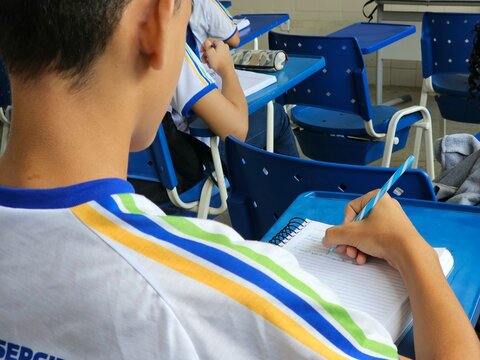 Aluno escrevendo no caderno durante aula em sala