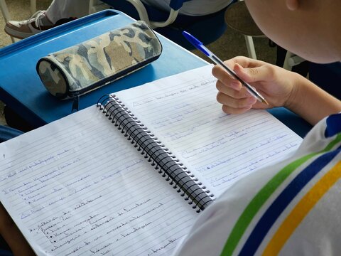 Aluno escrevendo no caderno durante aula em sala