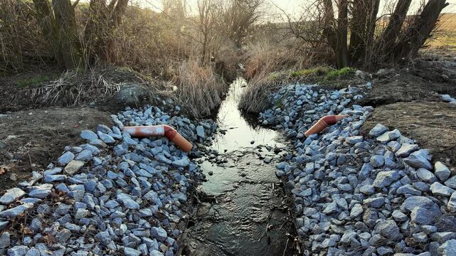 Professional riverbank stabilization using stone riprap and PVC drainage pipes, featuring gabion structures for erosion control, water management, and sustainable civil engineering solutions in natura