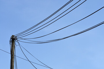 Fototapeta premium A weathered wooden utility pole stands against a clear blue sky with several black power lines stretching across the frame