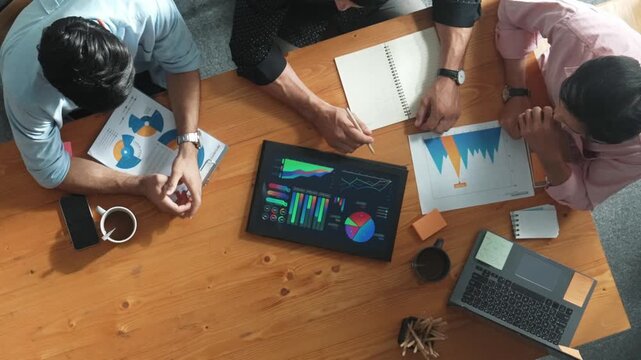 Executive manager explain financial graph to colleague at meeting room. Top aerial view of diverse marketing team sharing idea and planning strategy while sitting at table with tablet. Convocation.