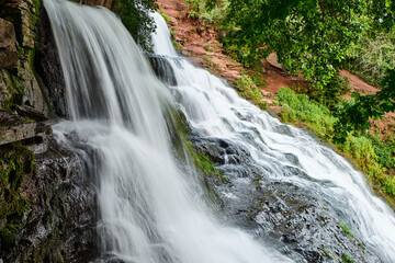 Fototapeta premium Beautiful multi-level Dzhuryn waterfall surrounded by lush green forest. Flowing water over rocks creates a serene natural landscape with a peaceful river and vibrant summer scenery