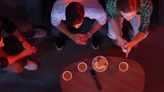 Happy family and colleague sitting at dark living room with red filter while cheering football team together. Caucasian people enjoy watching tv and giving high five and clinking glasses. Convocation.