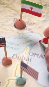 Conceptual image of a hand drawing a red line on a map of the Middle East with United States and Iran flags marking the Strait of Hormuz. Represents geopolitical conflict and global oil supply crisis.