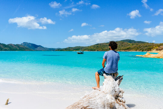 Man sitting on driftwood enjoying stunning Whitehaven Beach, Australia
