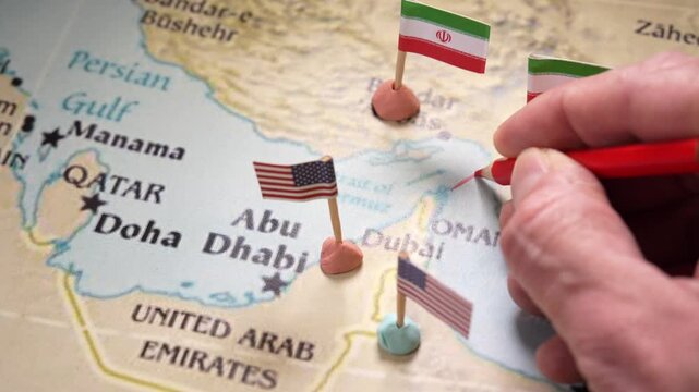 Military planner drawing a red line between Iran and Oman, illustrating a possible attack route through the Strait of Hormuz with flags representing the opposing forces of the US and Iran