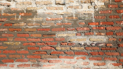 Old brick wall displaying a weathered mix of red, orange, and pale bricks with damaged mortar, creating a textured surface for background and architectural concepts © Newleks