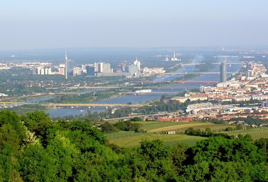 A breathtaking panoramic view of Vienna city and the Danube river from a high vantage point during a clear day. The landscape shows the blend of historic urban areas.