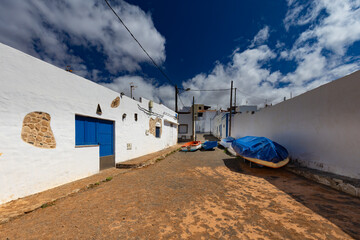 A traditional, whitewashed street lined with boats in the town of Ajuy, Fuerteventura, nestled on a black sand beach on the Atlantic Ocean. A background or wallpaper for your project © anettastar