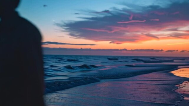A person watches sunset over calm ocean waves on a serene beach