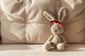 Fototapeta premium Plush Crocheted Bunny with Red Ribbon Sitting on Beige Couch