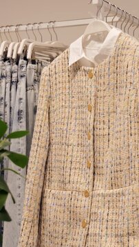 Elegant tweed blazer. Sophisticated boutique style featuring textured boucle fabric and gold buttons. Luxurious tweed coat displayed on rack with metallic buttons and elegant boutique setting