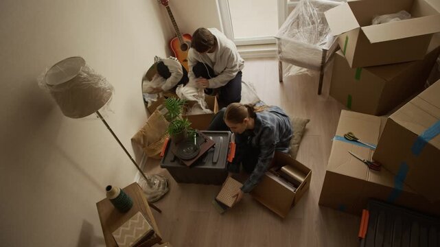 From above shot of young Caucasian couple unpacking cardboard boxes together in bright cozy living room during move into new apartment