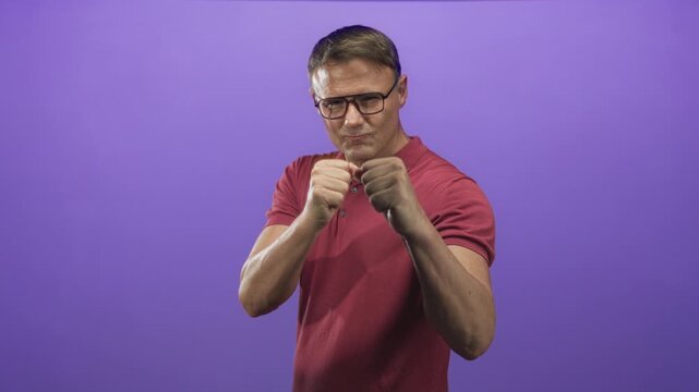 Man with fists raised and hands clenched in a boxing stance wearing glasses and red polo shirt in studio; training determination discipline.