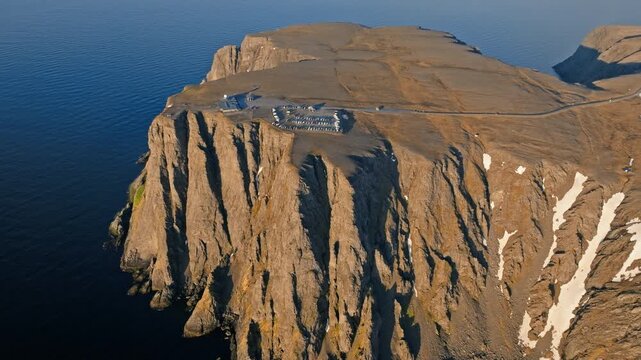 Aerial view flying along the steep North Cape cliffs on Mageroya Island, Norway. Dramatic Arctic rock formations rise above calm ocean waters.