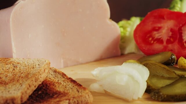 Wooden cutting board with bread, ham, onion, canned cucumber, sliced tomatoes and lettuce. Ingredient for prepare homemade fresh sandwiches. High quality 4k footage