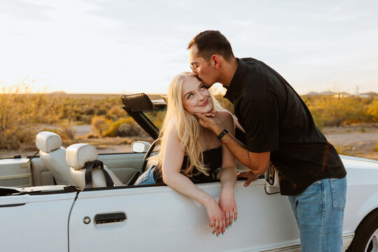 Boyfriend and girlfriend kissing in convertible during sunset